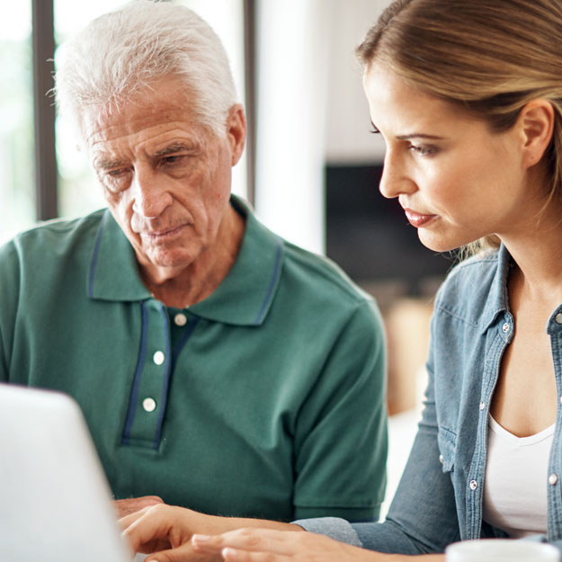 An older man and a younger woman look at the same computer screen. The woman has her hands on the keyboard.